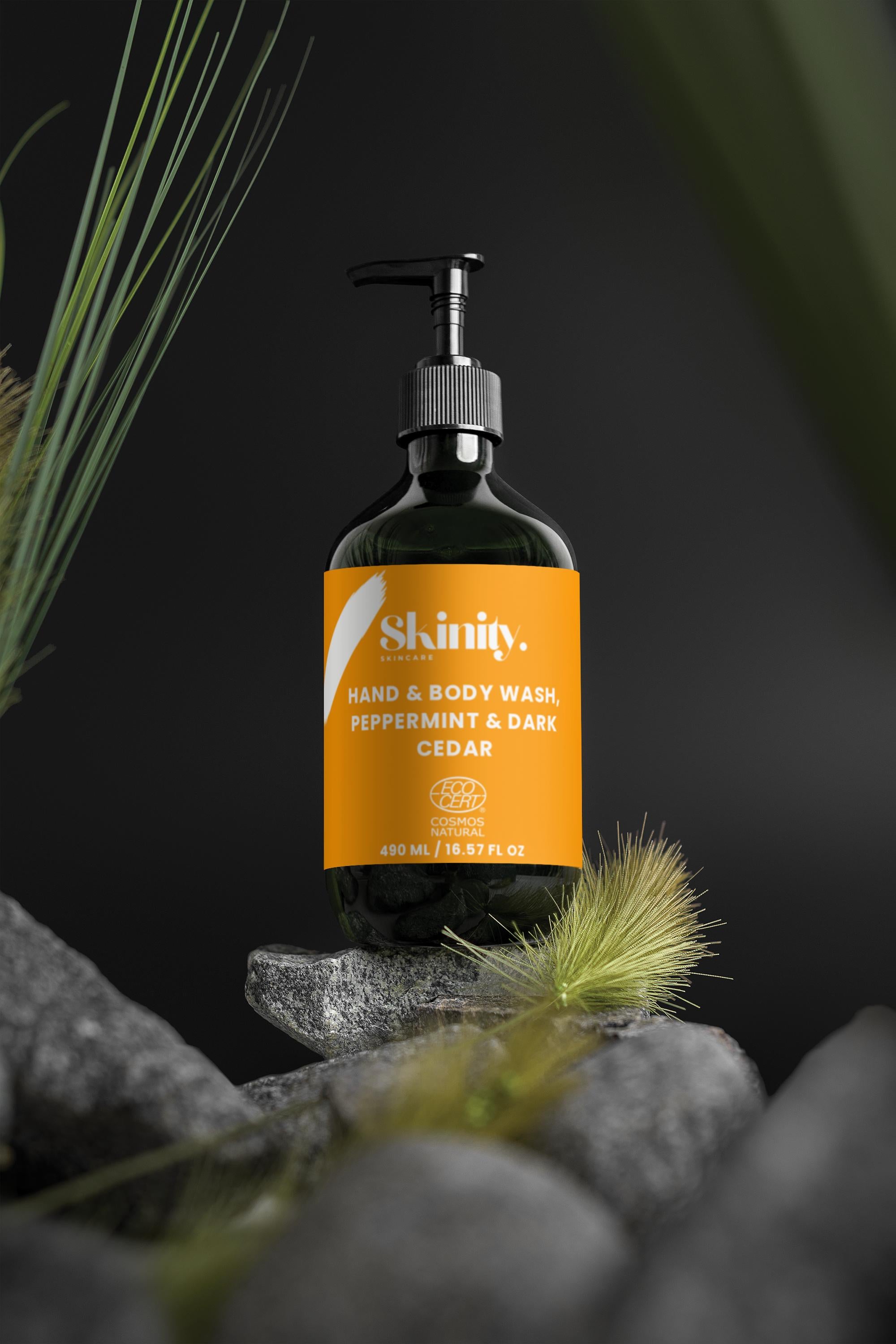 Hand and Body Wash Peppermint and Dark Cedar bottle with pump on stones and surrounded by green foliage.