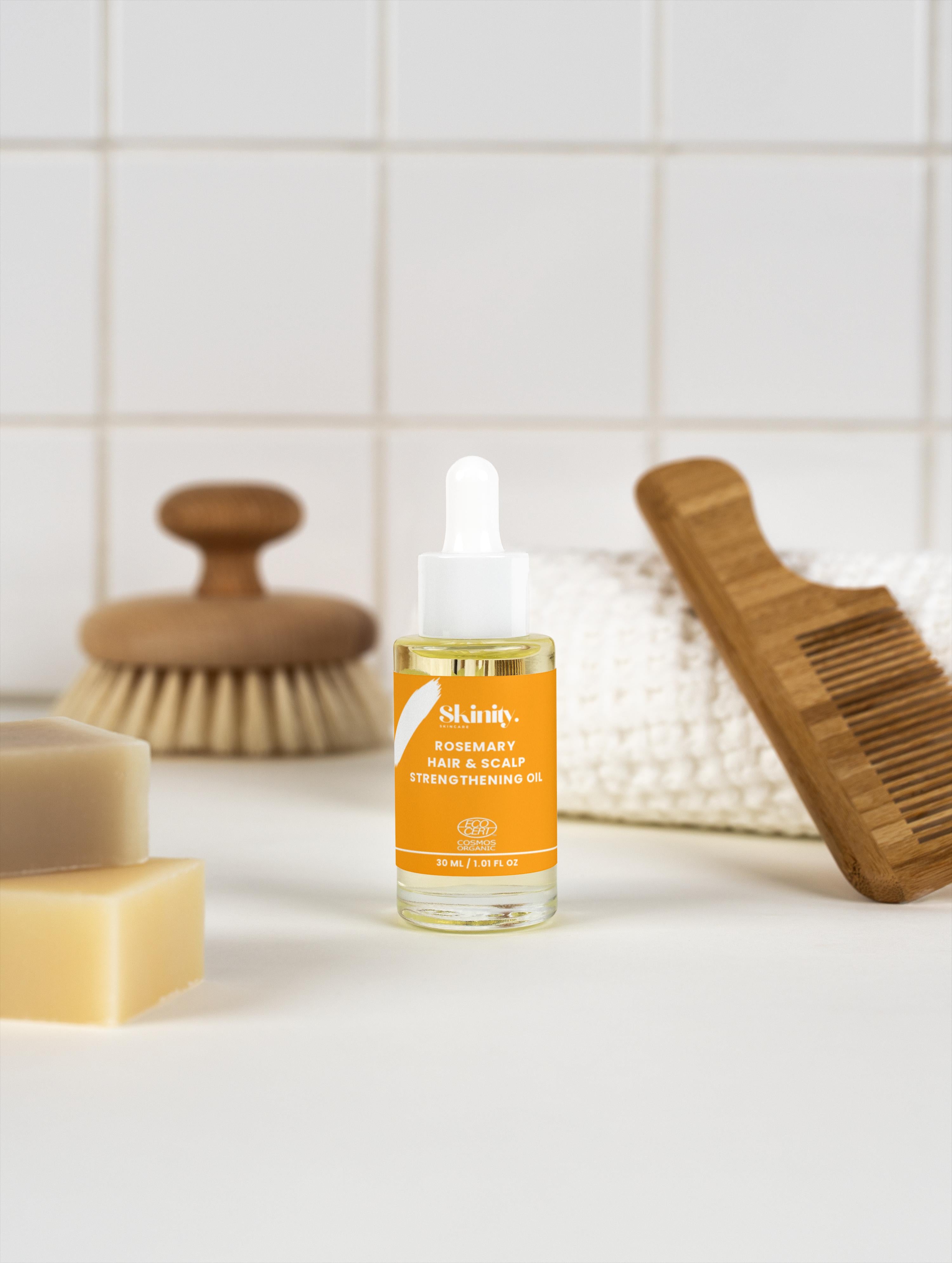 Rosemary Hair and Scalp Strengthening Oil bottle on a bathroom counter with soaps and a hairbrush.