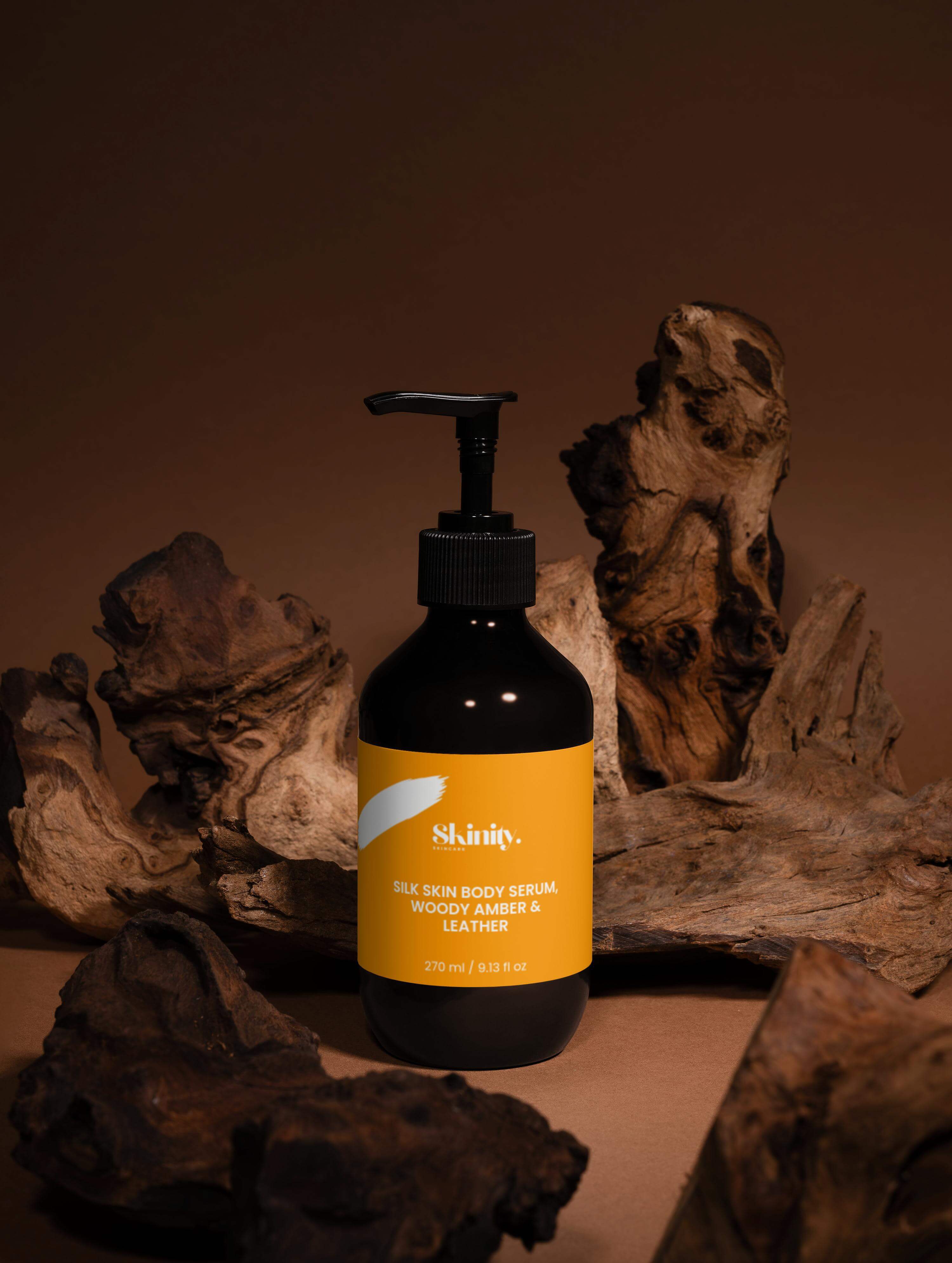 Silk Skin Body Serum Woody Amber and Leather in a pump bottle on a rustic wooden background.