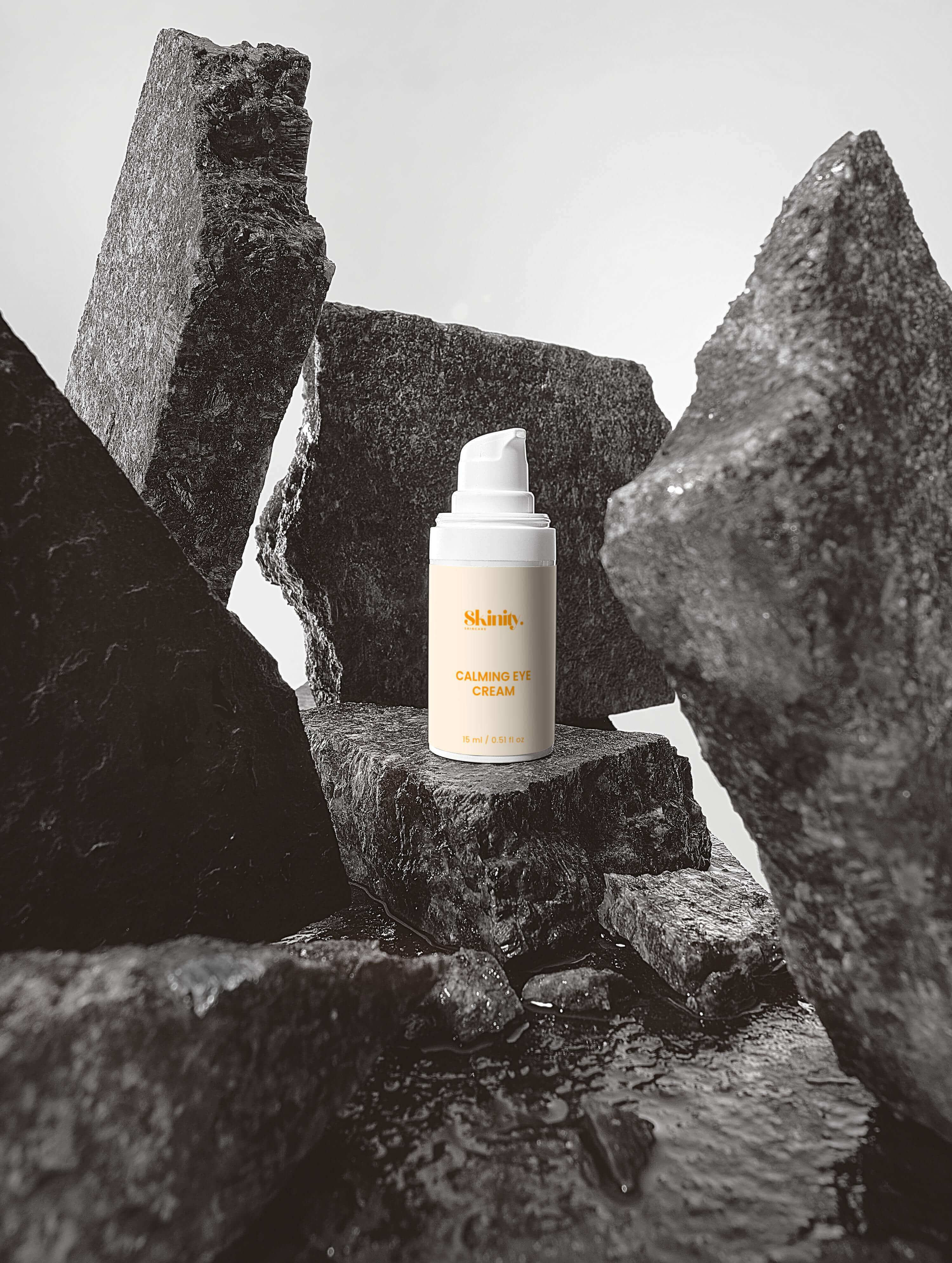 Calming Eye Cream for All Skincare bottle placed among large rocks, highlighting its natural and soothing qualities.