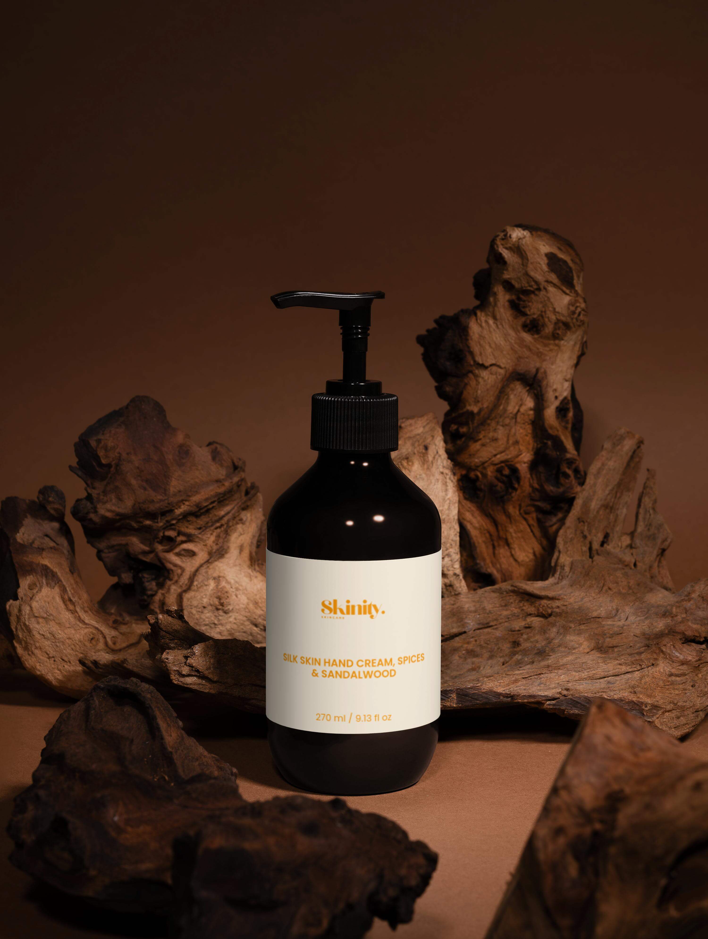 Silk Skin Hand Cream Spices and Sandalwood in a sleek black pump bottle on rustic wood backdrop.