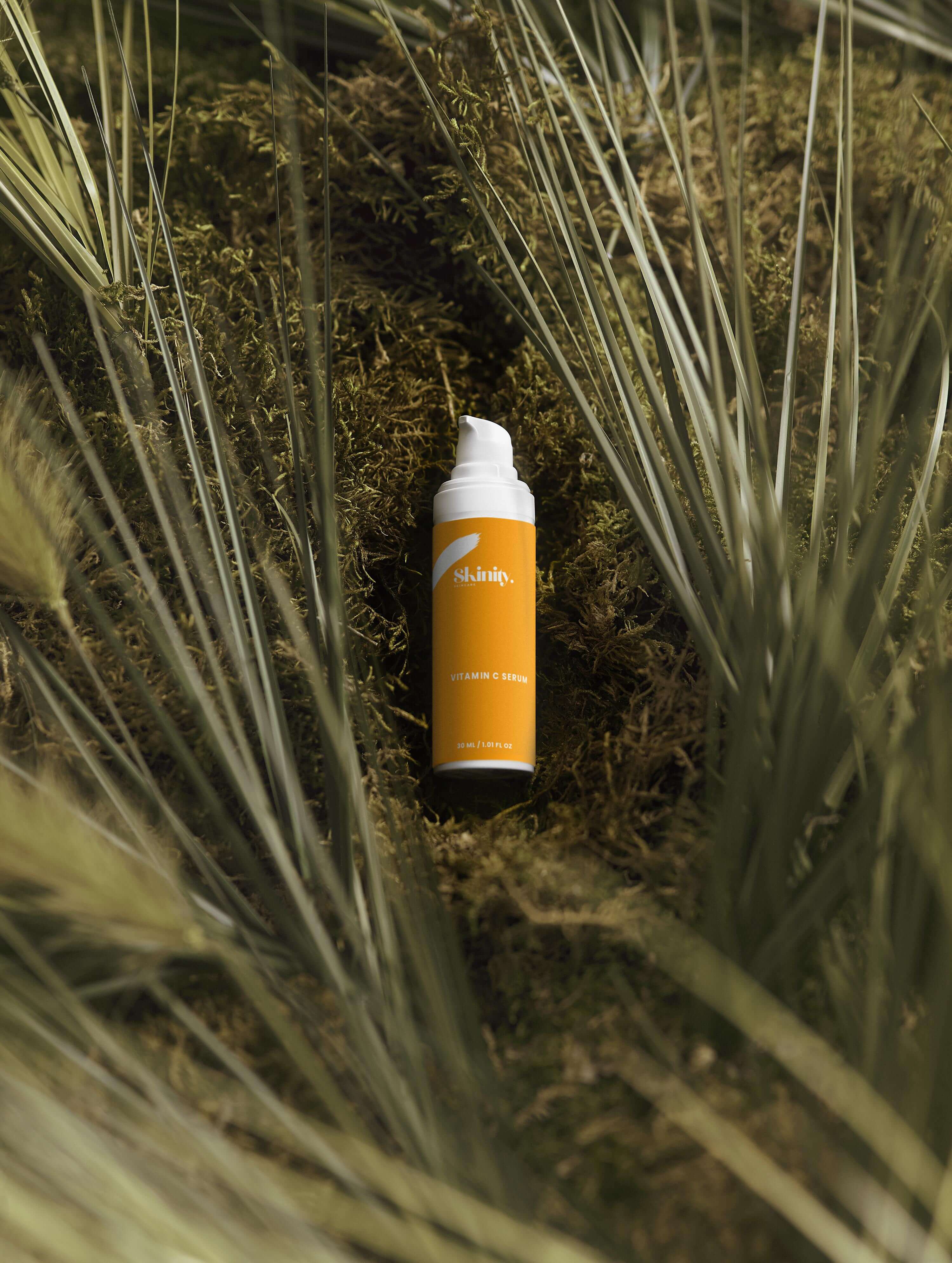 Vitamin C Serum for all skincare bottle surrounded by green foliage, promoting a rejuvenated and radiant complexion.
