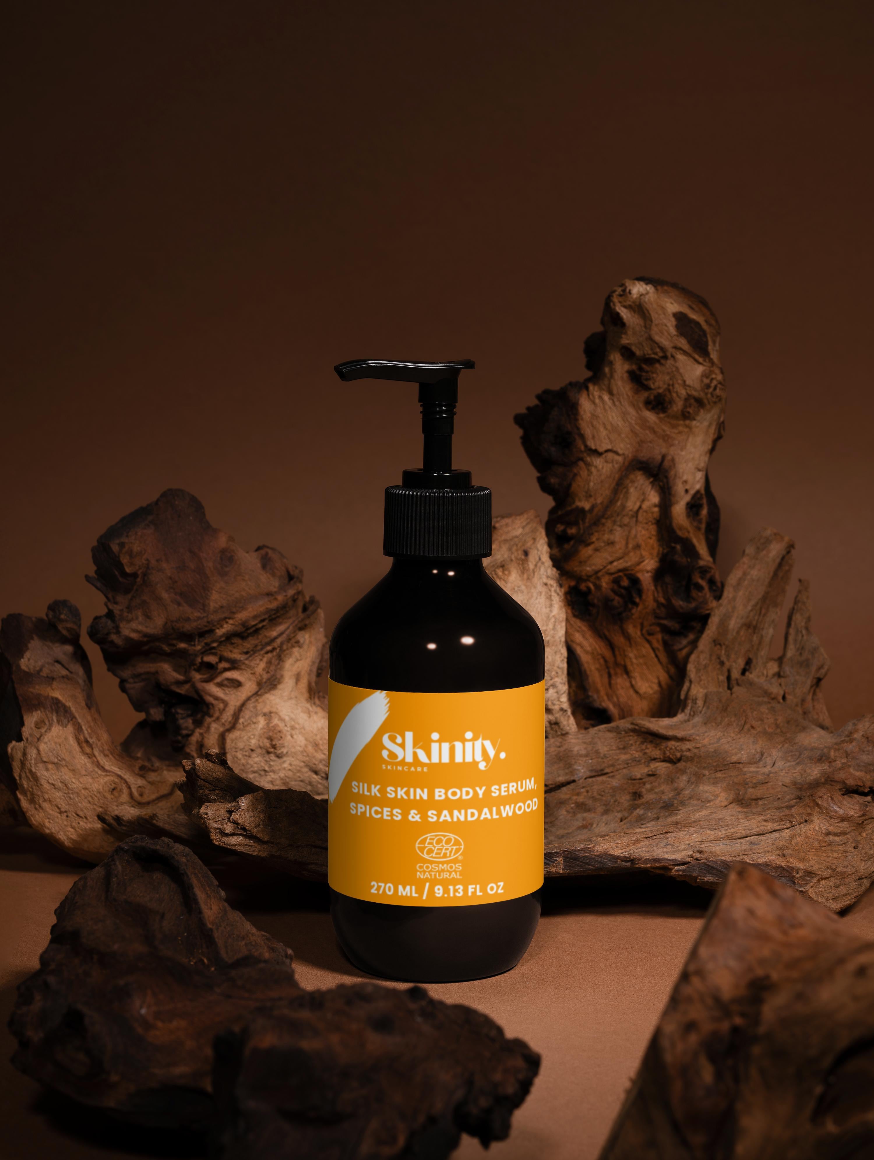 Silk Skin Body Serum Spices and Sandalwood in a black pump bottle on natural wood background.