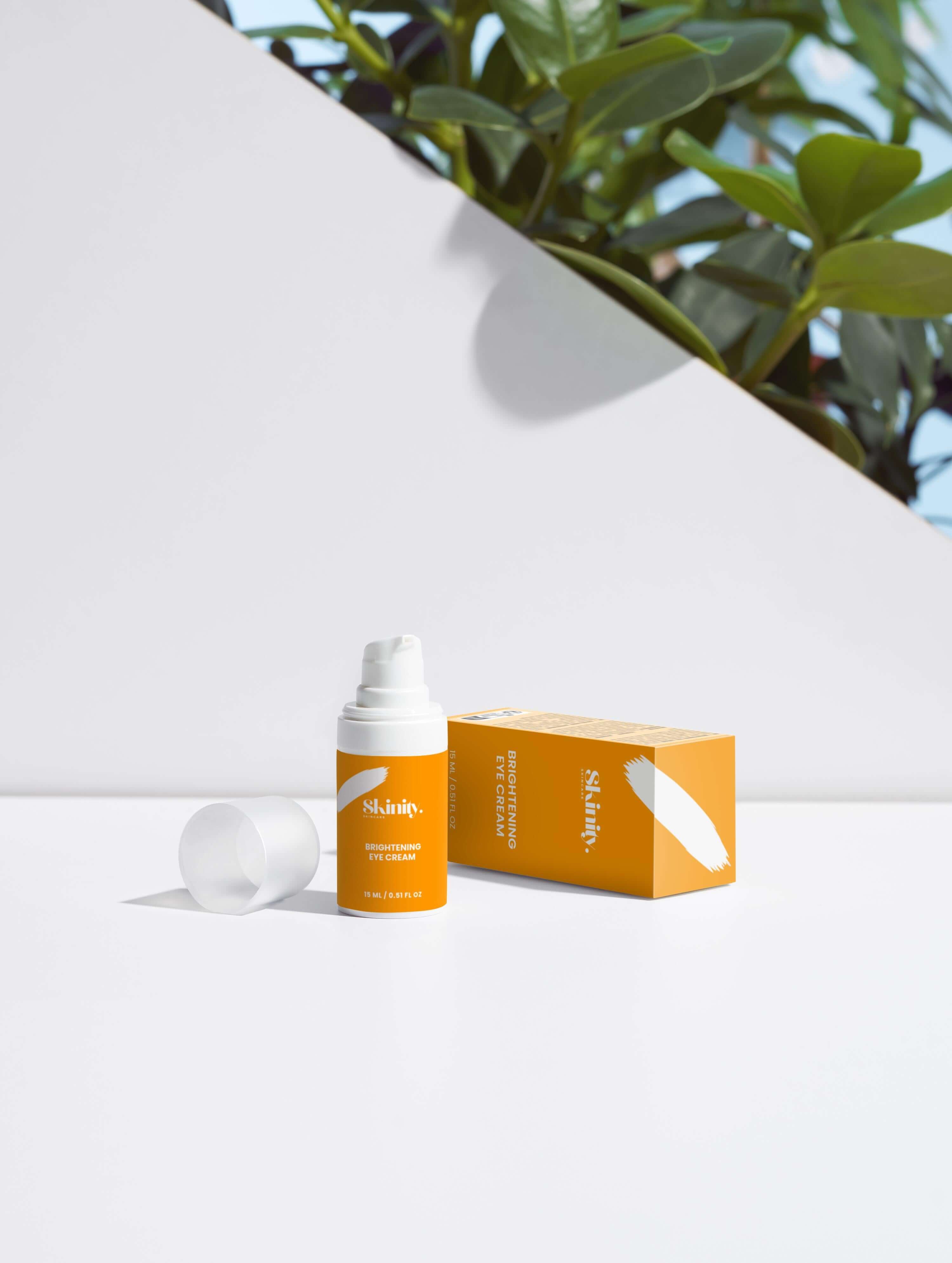 Brightening Eye Cream for All Skincare in a bright orange packaging with a plant backdrop.