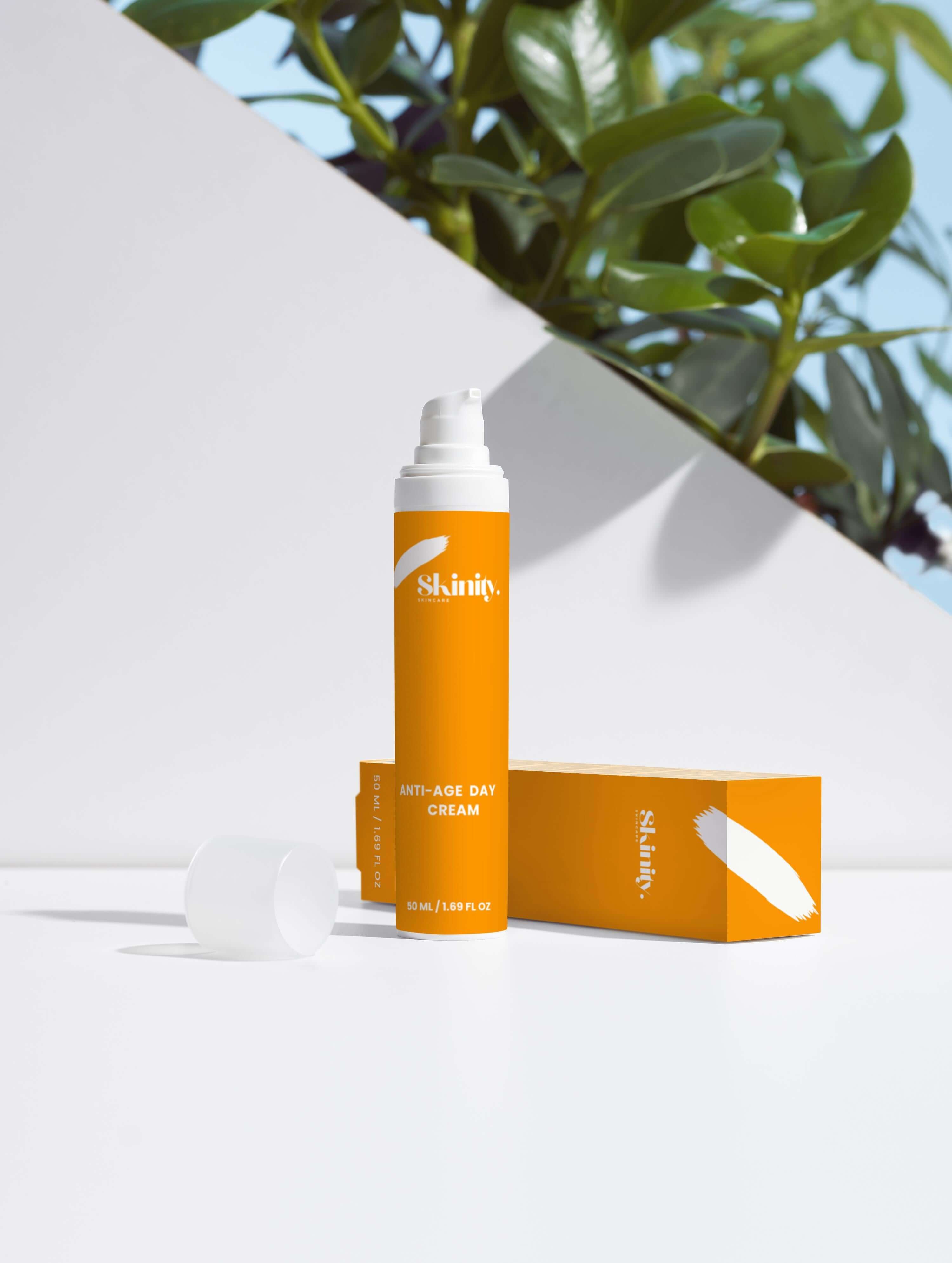 Anti-Age Day Cream For All Skin in an orange bottle with a box, placed on a white surface with green leaves.