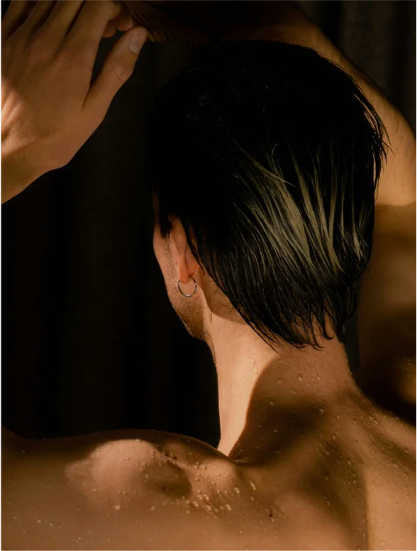 Man with wet hair in shower, showcasing the use of Deep Cleanse Scalp Scrub Rosemary and Mint for a refreshed scalp.