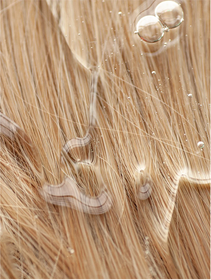 Close-up of healthy, shimmering hair with water droplets showcasing the benefits of Keratin Volume Boost Conditioner.
