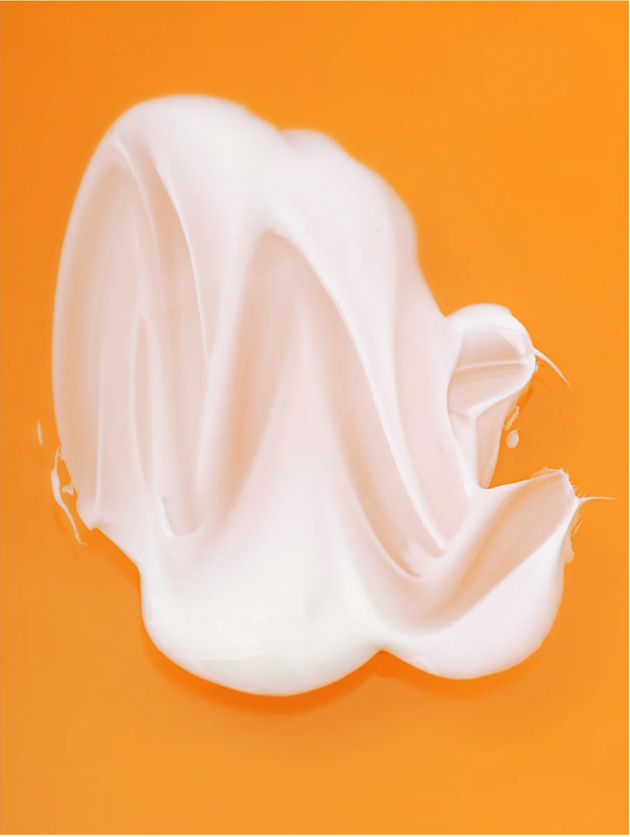Creamy texture of a Retinol Alternative Moisturizer on an orange background.