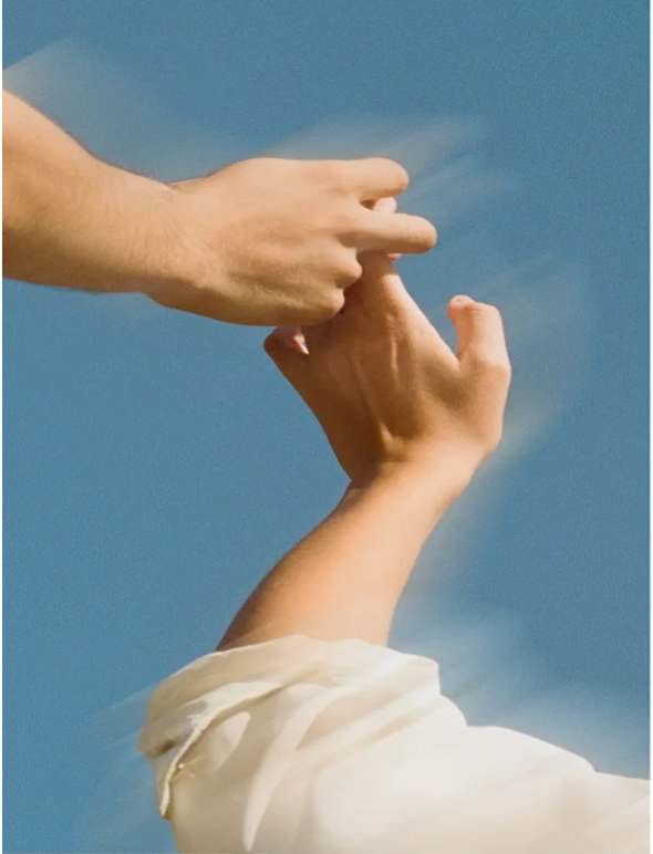Two hands reaching for each other against a clear blue sky, symbolizing connection and support.