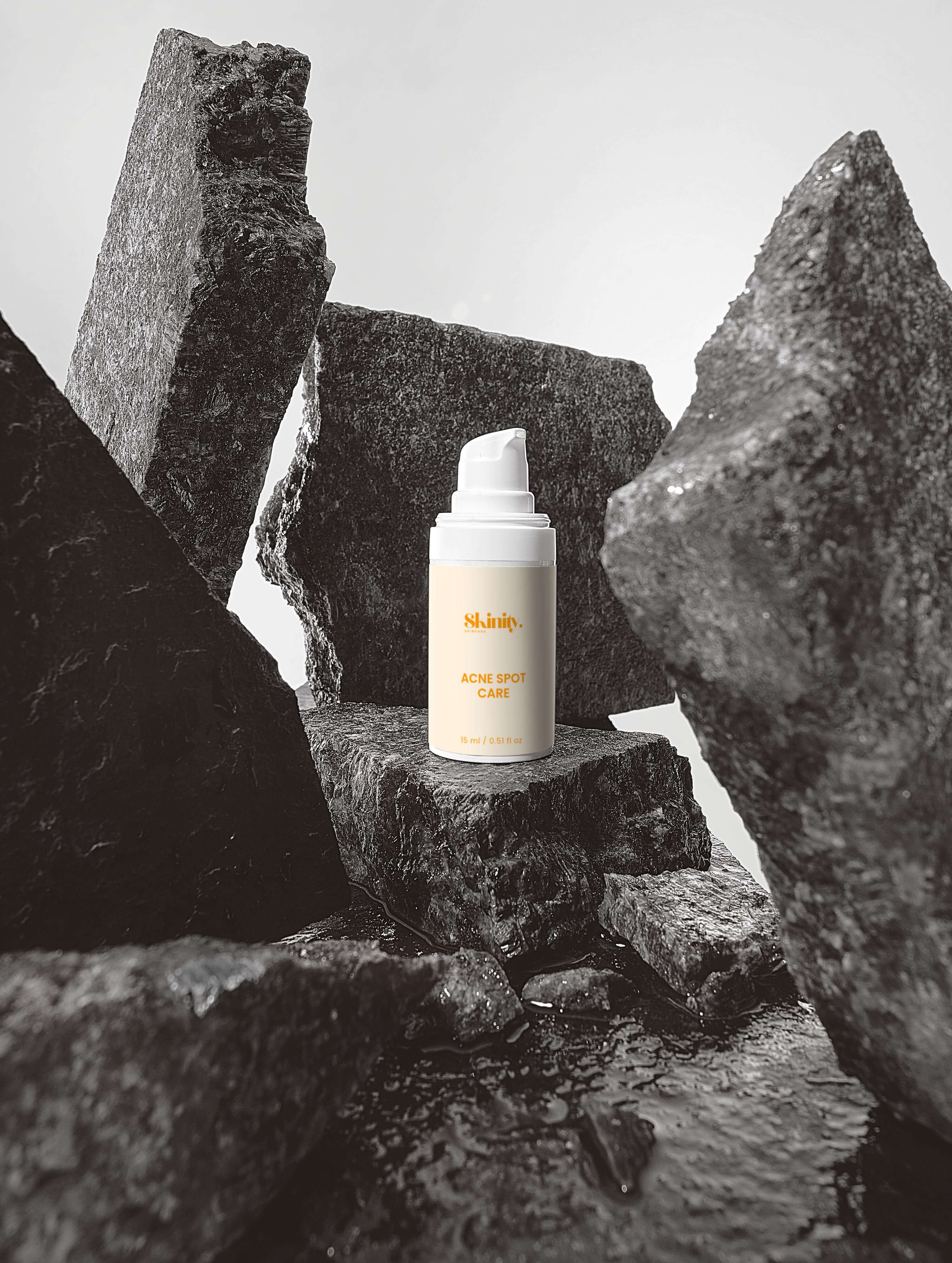 Acne Spot Care Serum for all skin types displayed on textured stones in black and white.