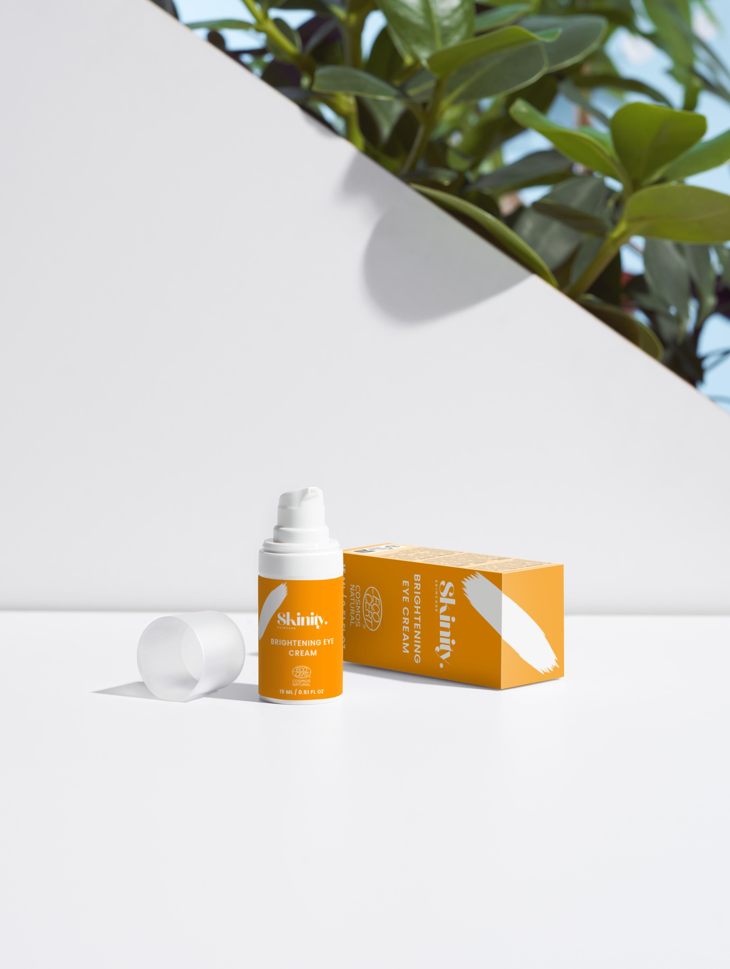 Brightening Eye Cream for All skincare on a white surface with a plant in the background, showcasing the eco-friendly packaging.